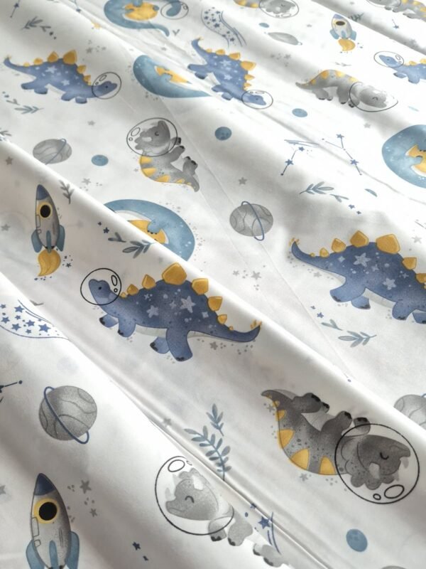 Tela sarga con estampado de dinosaurio espacial y cohetes dispuesta en forma de olas