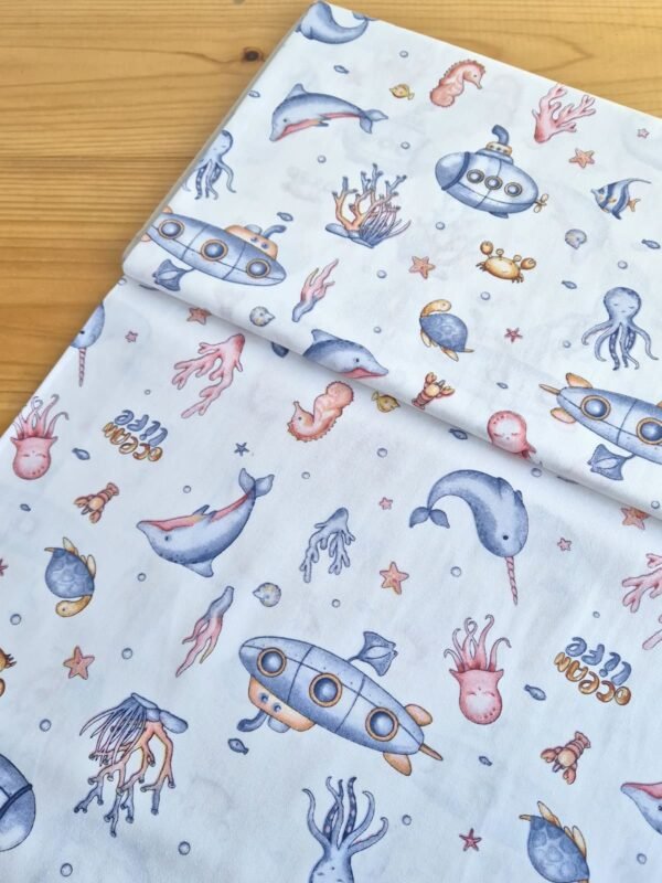 Tela sarga con estampado de vida marina sobre fondo blanco, vista en ángulo para mostrar textura y caída del tejido