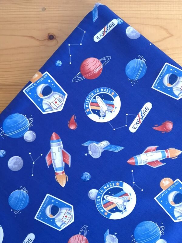 Tela sarga con estampado de astronautas y planetas sobre fondo azul vista desde arriba