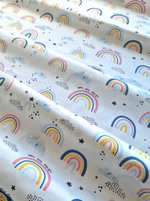 Tela sarga con estampado de arcoíris, nubes y la frase Follow Your Dreams en fondo rosa dispuesta en forma de olas