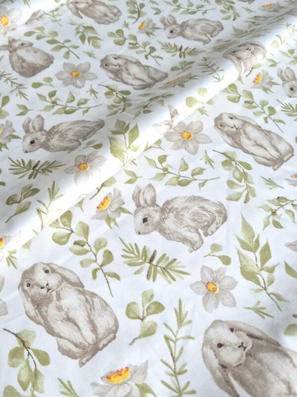 Tela sarga con estampado de conejos y ramas verdes dispuesta en forma de olas