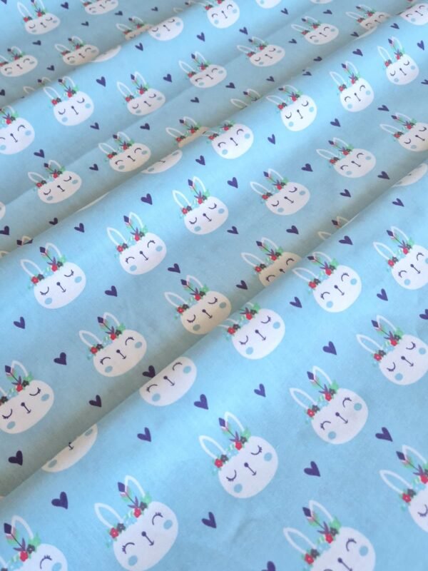 Tela sarga con estampado de caras de conejos con plumas sobre fondo celeste dispuesta en forma de olas