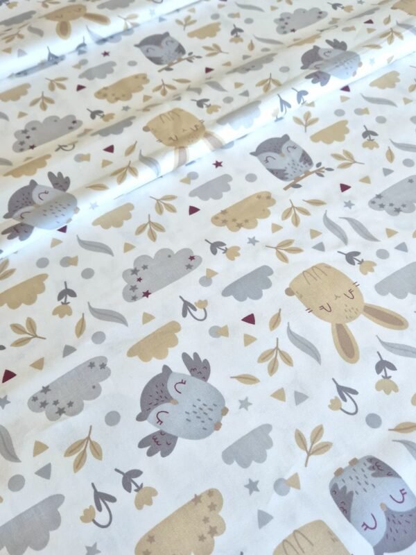 Tela sarga con estampado de conejos, búhos y nubes sobre fondo blanco dispuesta en forma de olas