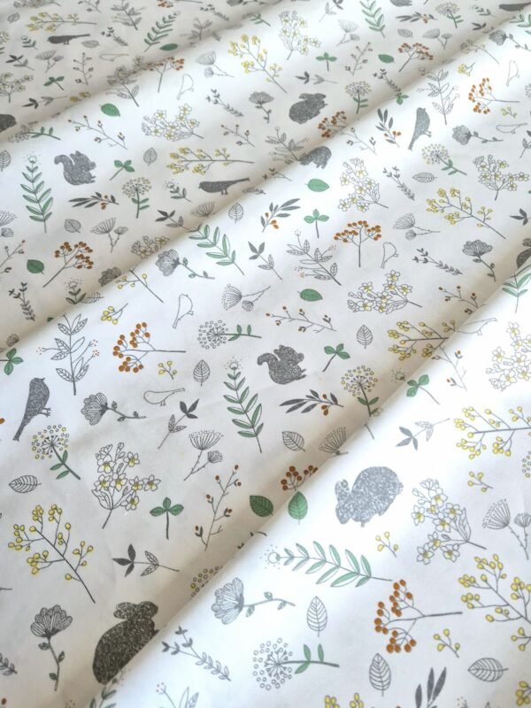 Tela sarga con estampado de conejos y flores silvestres sobre fondo blanco dispuesta en forma de olas