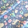Tela sarga con estampado de conejos y flores sobre fondo azul oscuro dispuesta en forma de olas