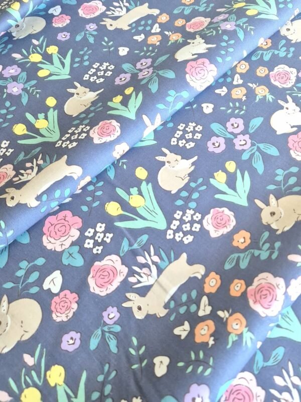 Tela sarga con estampado de conejos y flores sobre fondo azul oscuro dispuesta en forma de olas