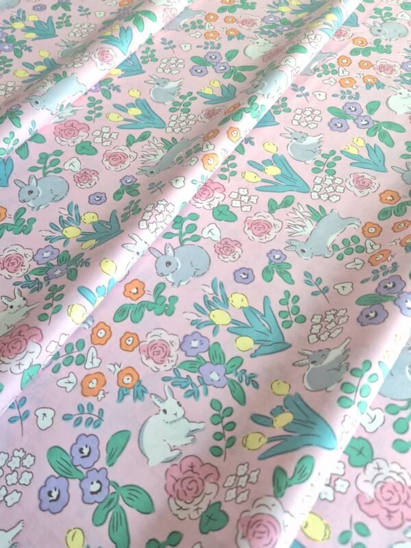 Tela sarga con estampado de conejos y flores sobre fondo rosa dispuesta en forma de olas