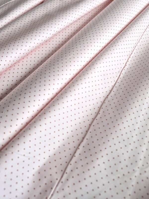 Tela sarga rosa pálido con lunares pequeños dispuesta en ondas para mostrar caída y textura