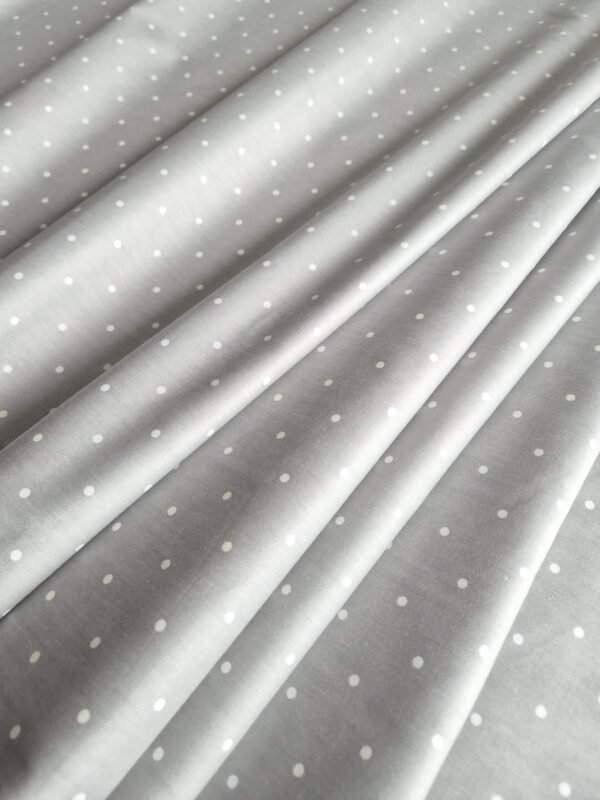 Tela sarga gris con lunares blancos, dispuesta en ondas para mostrar textura y caída