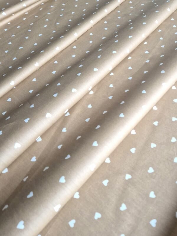 Tela Sarga con corazones blancos en fondo beige oscuro doblada en forma de olas