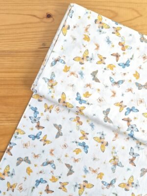 Vista superior de tela sarga con estampado de mariposas naranjas y azules sobre fondo blanco