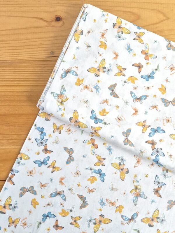 Vista superior de tela sarga con estampado de mariposas naranjas y azules sobre fondo blanco