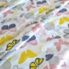 Tela sarga con estampado de mariposas en tonos suaves sobre fondo blanco dispuesta en forma de olas