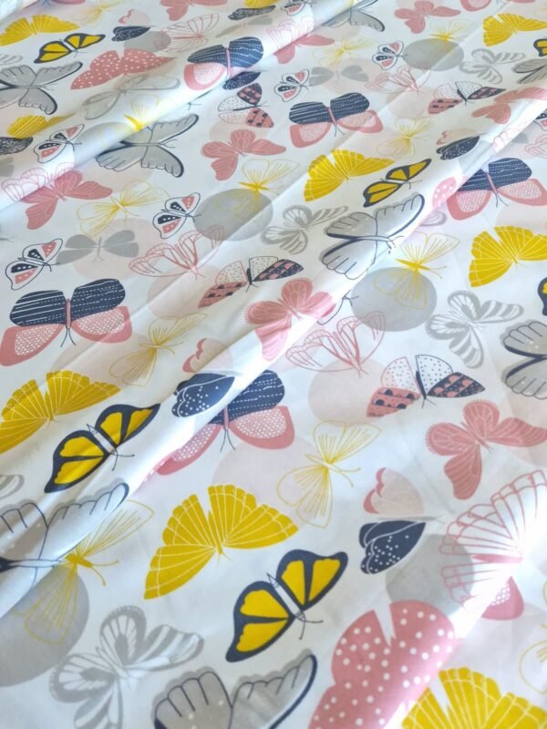 Tela sarga con estampado de mariposas en tonos suaves sobre fondo blanco dispuesta en forma de olas