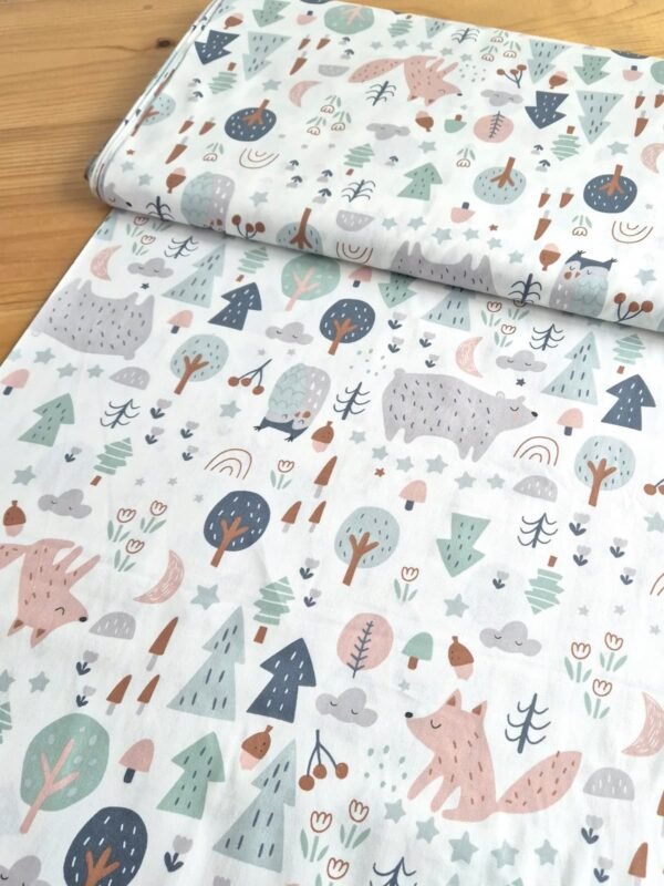 Tela sarga con estampado de animales del bosque y naturaleza sobre fondo blanco, vista en ángulo para mostrar textura y caída del tejido