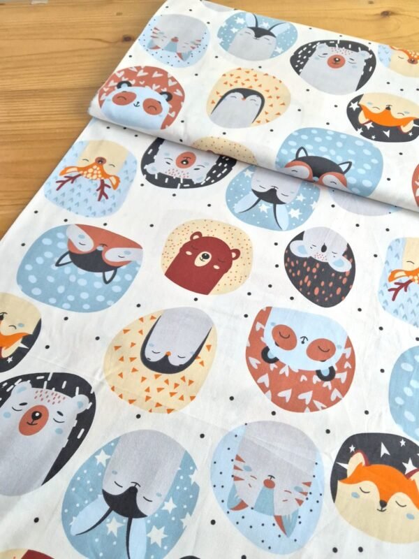 Tela sarga con estampado de caras de animales en círculos sobre fondo blanco, vista en ángulo para resaltar textura y caída del tejido