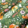 Tela sarga con estampado de zorro y flores del bosque sobre fondo verde dispuesta en forma de olas