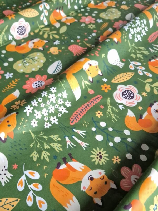 Tela sarga con estampado de zorro y flores del bosque sobre fondo verde dispuesta en forma de olas