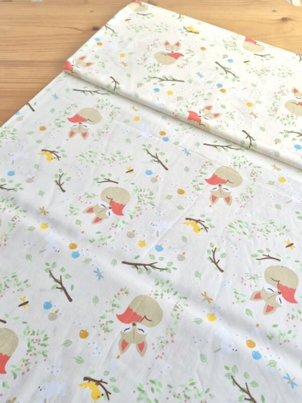 Tela sarga con estampado de zorros dormidos entre árboles sobre fondo claro, vista en ángulo para mostrar textura y caída