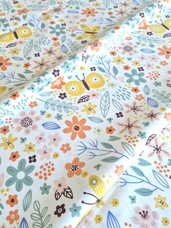 Tela sarga con estampado de flores y mariposas de jardín dispuesta en forma de olas