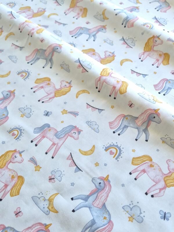 Tela sarga con estampado de unicornios y arcoíris en tonos rosas dispuesta en forma de olas