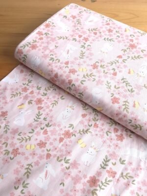 Tela sarga con estampado de conejos y mariposas en campo de flores vista en ángulo de 45 grados