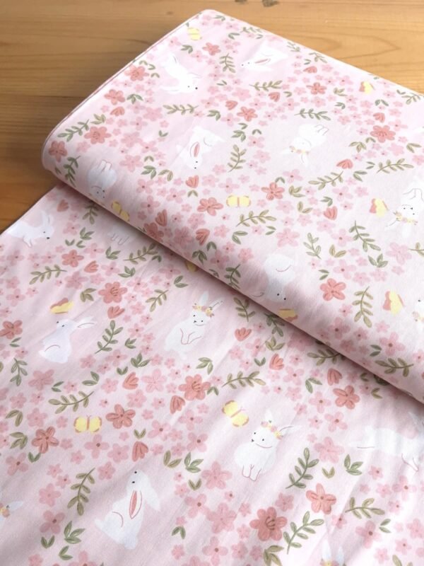 Tela sarga con estampado de conejos y mariposas en campo de flores vista en ángulo de 45 grados